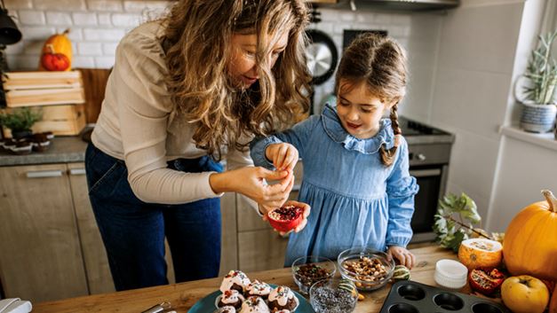 A mother and daughter stand by their dining room table and add decorations to their recent bakes