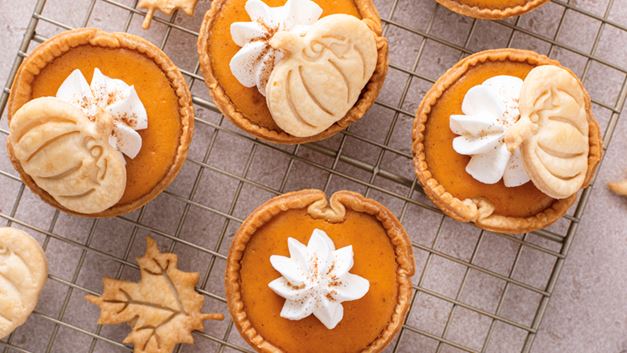 Mini pumpkin pies with whipped cream decor cooling on a wire baking stand