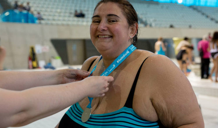 Smiling woman at Swimathon 2018 in support of Marie Curie and CRUK receiving her medal