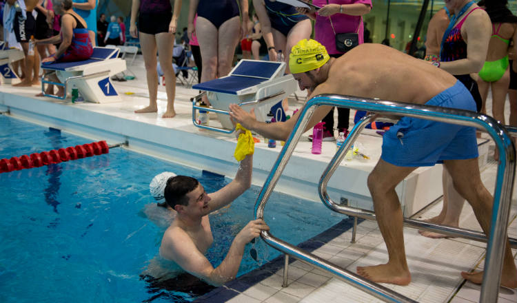 A swimmer receives encouragement from a teamate as he finishes a length at Swimathon 2018 in support of Marie Curie and CRUK 